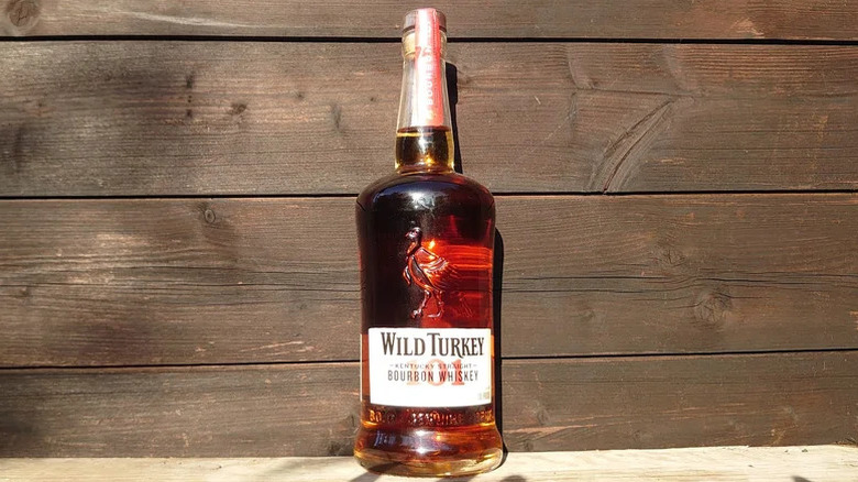 The sun shining on a bottle of Wild Turkey 101 posed in front of a wooden background