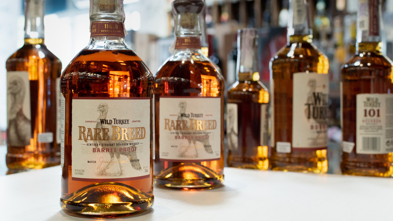Two bottles of Wild Turkey Rare Breed on a table with other blurred bottles in the background
