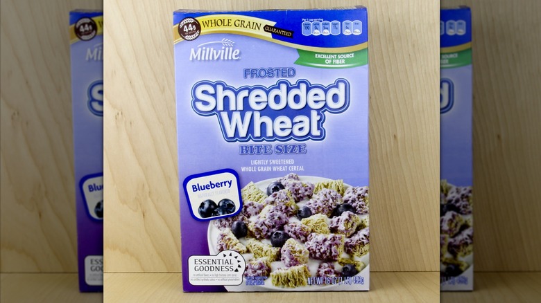 A box of Millville Blueberry Frosted Shredded Wheat cereal against a light wooden backdrop.