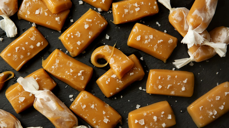 Caramels both in and out of their wax paper wrappers on a black background