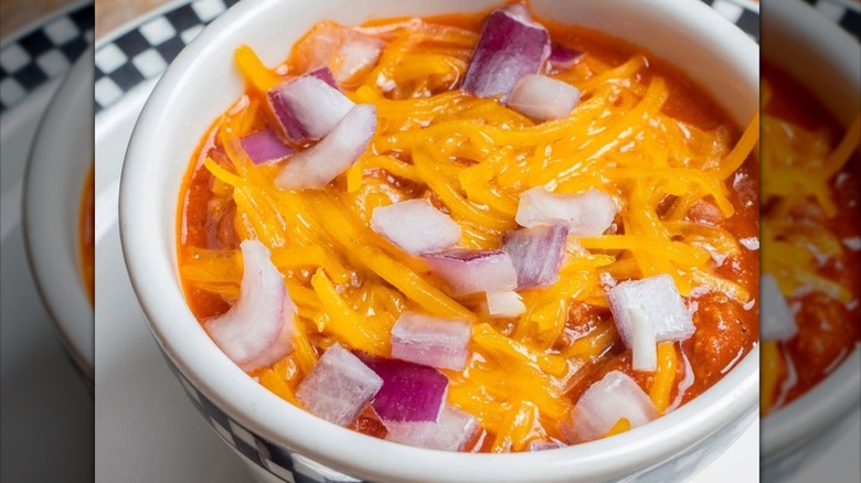 A bowl of chili covered in melted cheese and red onion
