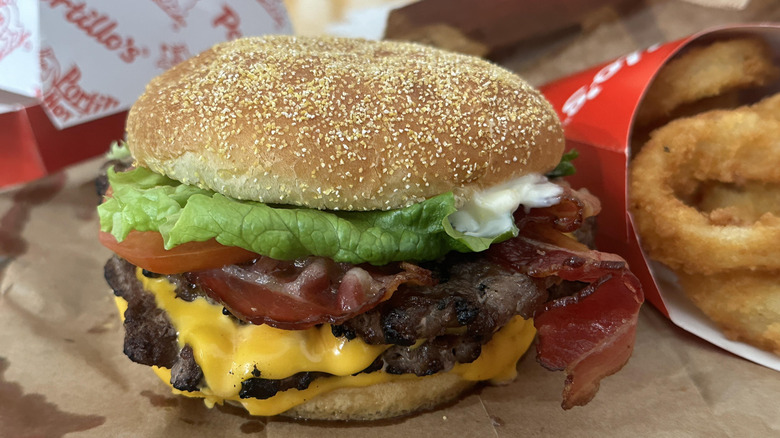 A double cheeseburger from Portillo's with some onion rings sitting on paper