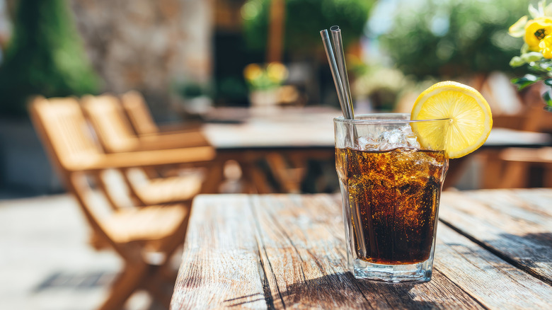 Outdoor seating and wooden table with a soda in a glass on top