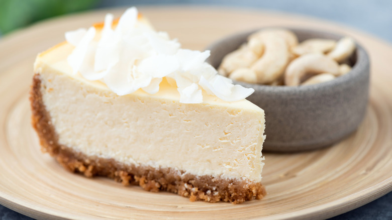Cashew cheesecake with a bowl of cashews in the background on a tan plate