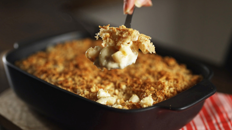 Baked mac and cheese in a cast-iron pan getting scooped out