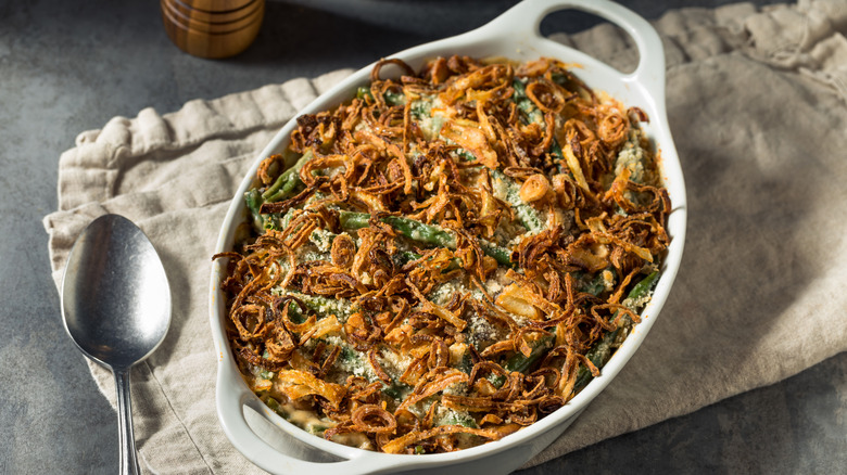 Green bean casserole in a white dish on a linen cloth with a spoon on the side