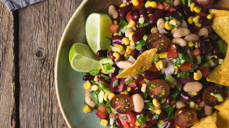 Cowboy Caviar with corn chips and lime wedges in a green bowl