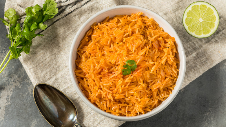 Red rice in a white bowl on a linen cloth with a lime and parsley