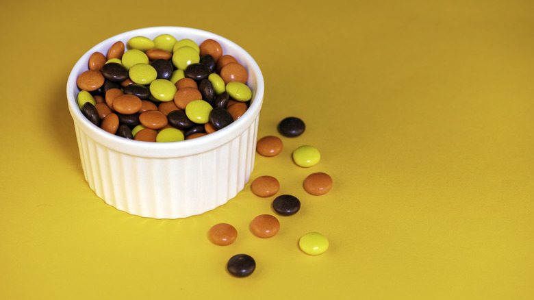 Reese's Pieces in small white bowl on yellow surface