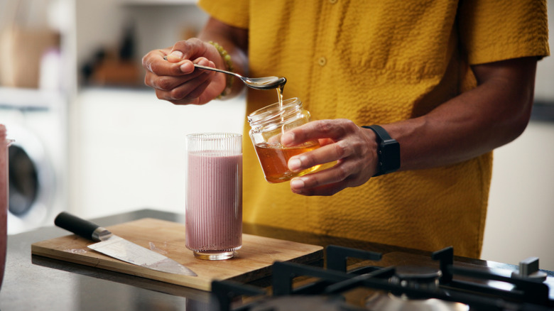 man adding honey to smoothie
