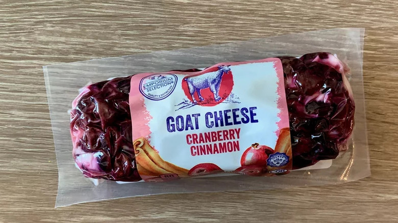 A package of Emporium Selection Goat Cheese with cranberry and cinnamon flavor is displayed on a wooden surface