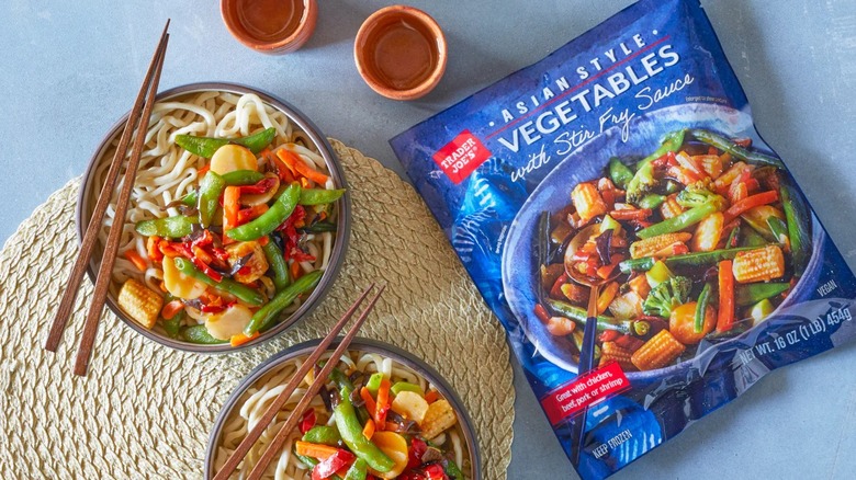 A bag of Trader Joe's Asian Style Vegetables with Stir Fry Sauce next to two prepared bowls with chopsticks
