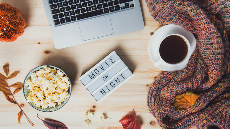 fall leaves, popcorn, coffee, a cozy blanket, a computer, and a sign that says 