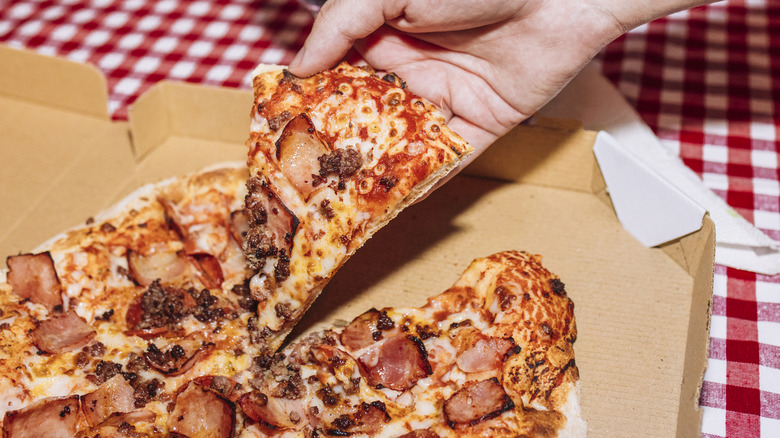 person taking a slice of pizza out of a pizza box