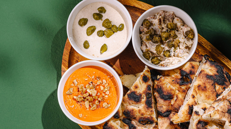 various dips on a wooden cutting board with pita bread