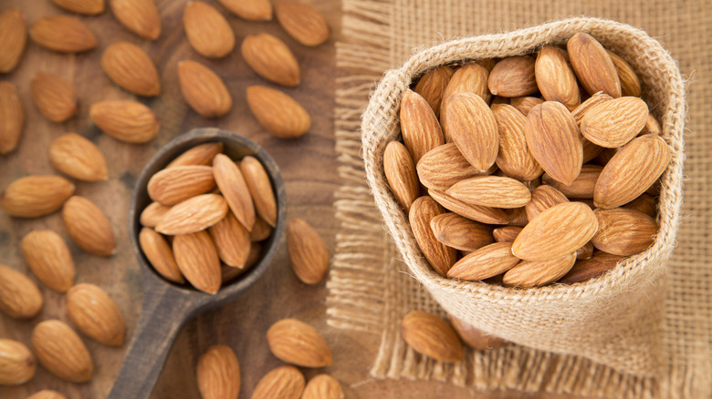 hessian bag and scoop of raw almonds on wooden background