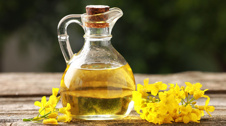 small glass jug of canola oil with canola flowers