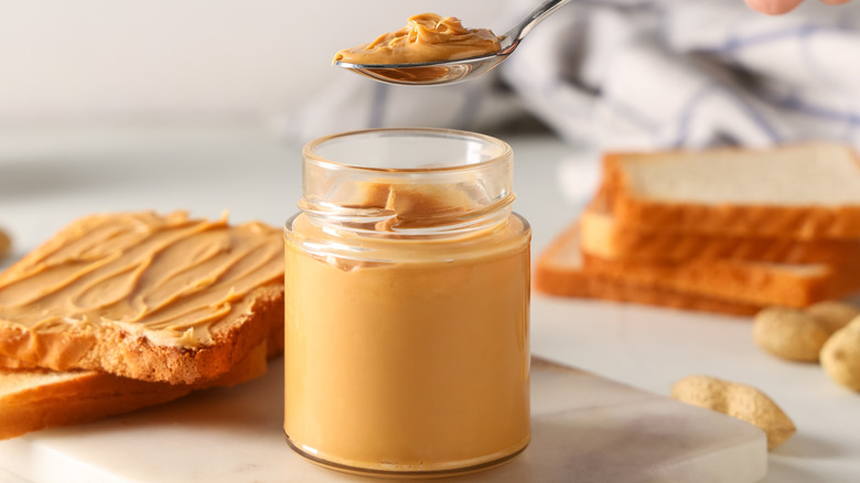 spoon of peanut butter in jar with bread in background