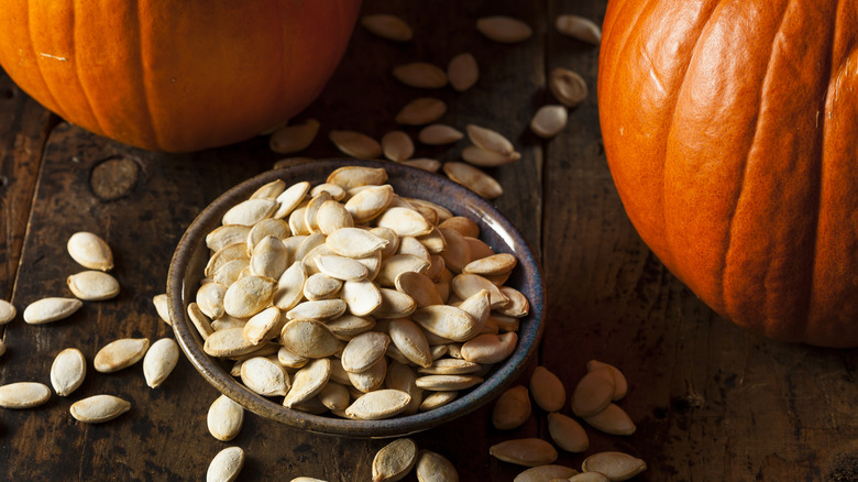 glass bowl of pumpkin seeds in the shell with whole pumpkins