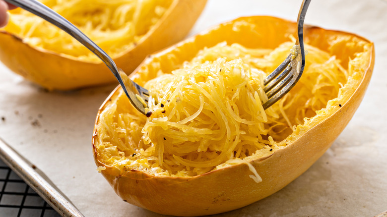 Baked spaghetti squash halves with forks removing strands from the inside