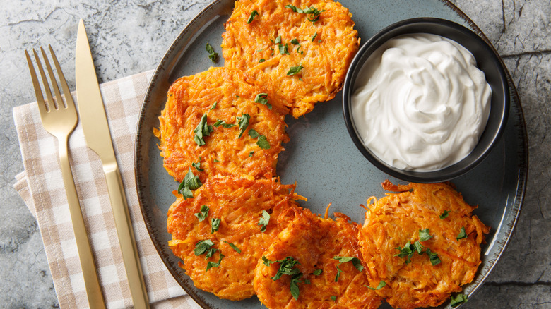 Sweet potato fritters on plate with bowl of sour cream, next to napkin and cutlery