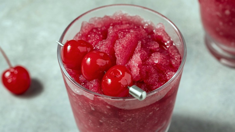 Dark red cherry slush drink in glass with garnish of maraschino cherries on skewer