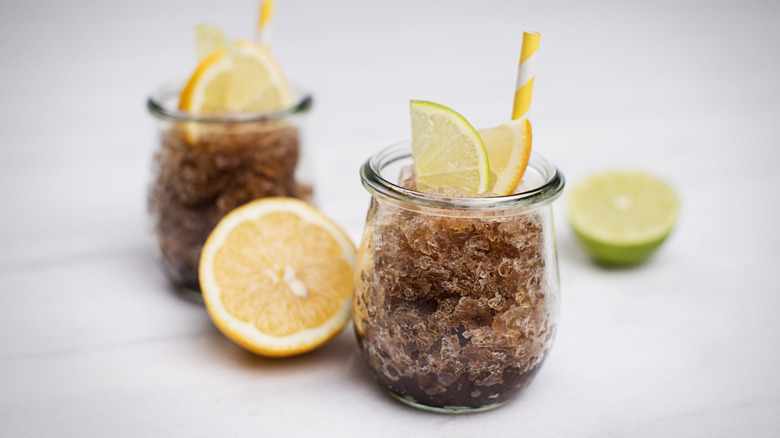 Two rounded glasses full of cola slush garnished with lime and lemon wedges