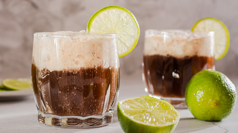 Two short glasses of dirty soda cola mixed drink garnished with lime wheels