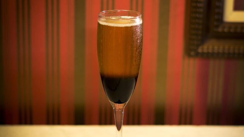 Champagne flute full of light and dark alcohols against red and black striped background