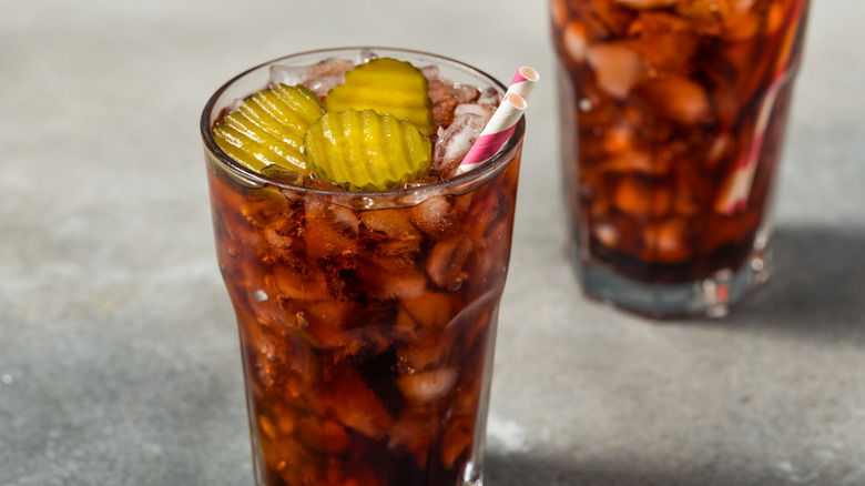Glass of Coca-Cola with pickle chips and red and white striped straw