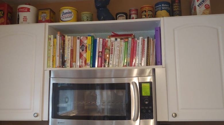Cookbooks stacked above microwave in kitchen.