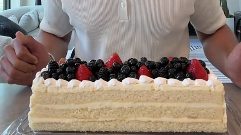 Man behind Member's Mark sweet fruit topped Chantilly cream bar cake on countertop