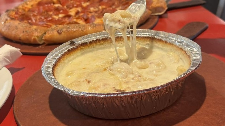 A foil tray of gooey, cheesy mac and cheese with a fork lifting some out