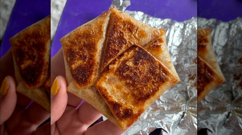A person holding a creme brulee Crunchwrap slider over a foil wrapper