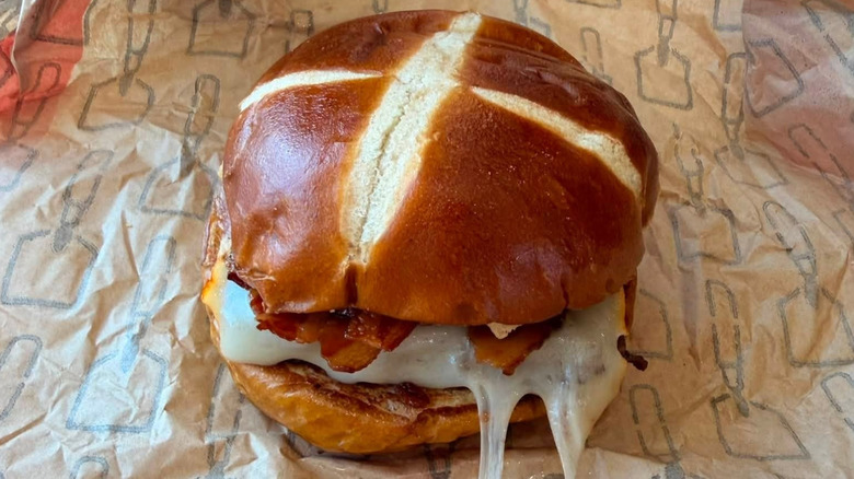 A Wendy's Pretzel Bacon Pub Burger with visible bacon and melty cheese sitting in a paper wrapper