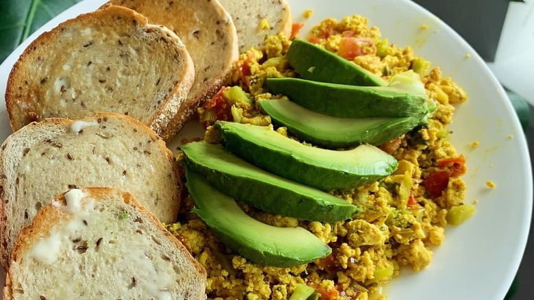 Plate of tofu scramble with green onions, broccoli, tomato, avocado, and caraway rye toast at Apothecary Kitchen