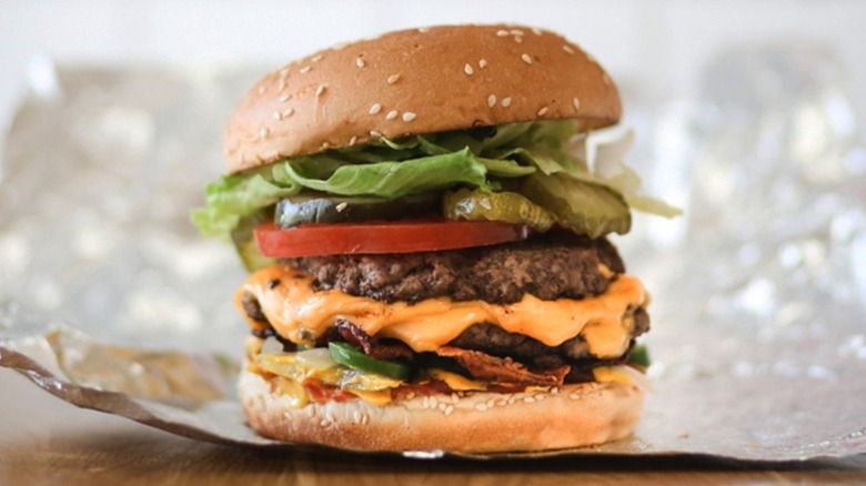 Five Guys Bacon Cheeseburger sitting on a foil wrapper on a wooden table