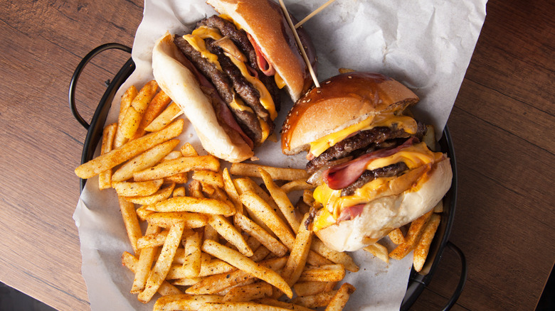 A couple of cheeseburgers in a paper-lined black metal basket with french fries on a wooden background