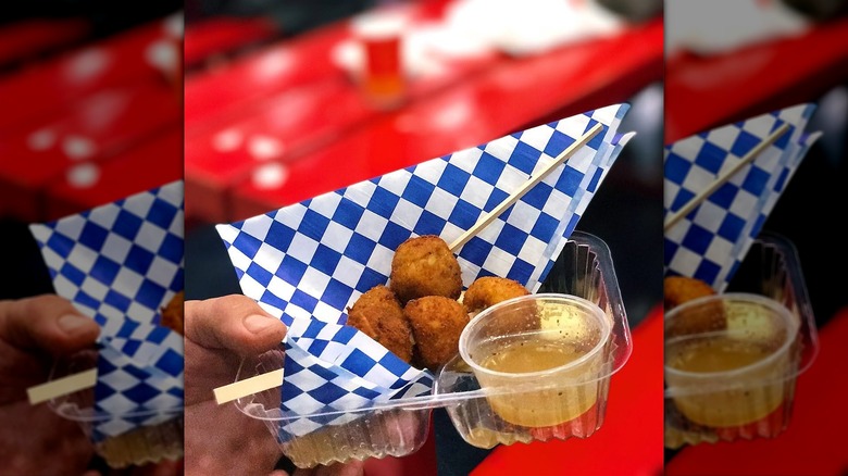 Hand holding deep-fried chicken noodle soup on a stick in plastic container with blue and white packaging, mirrored image