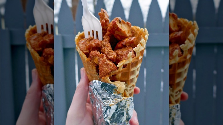 Hand holding fried chicken in a waffle cone in front of blurred blue background