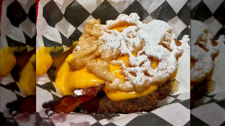 Mirrored image of funnel cake bacon queso burger on checked paper with blurred background