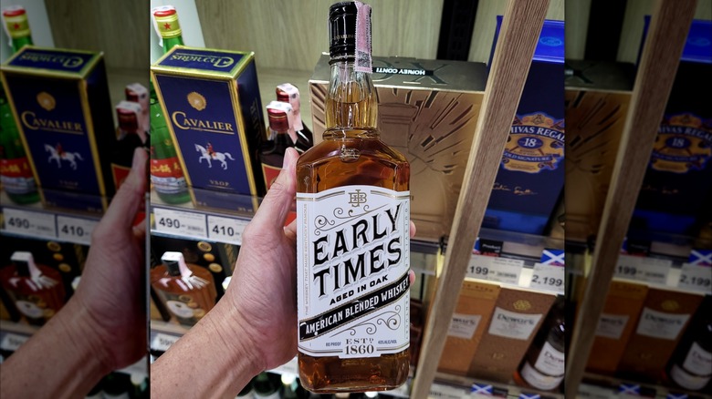 A person holding a bottle of Early Times to the camera in a liquor store
