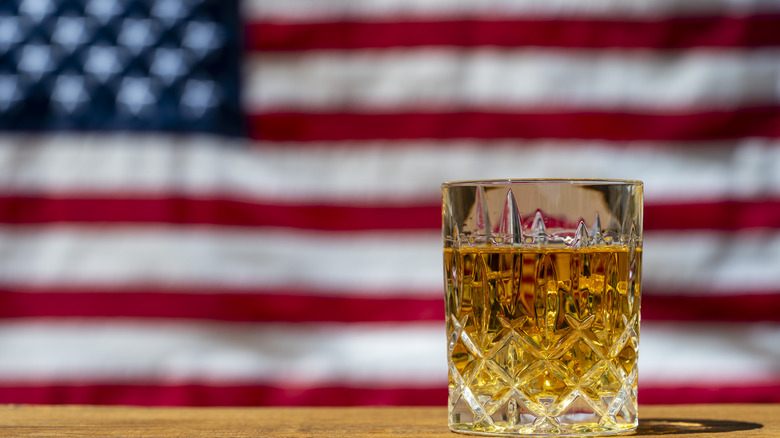 A glass of bourbon posed in front of a blurred American flag