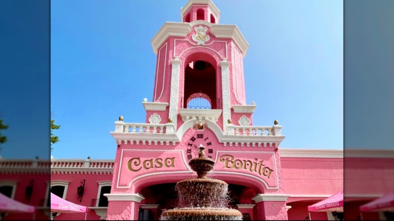 Bright pink exterior of Casa Bonita with bell tower, fountain, and blue sky