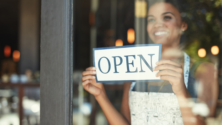 Smiling person hanging an "open" sign in the window