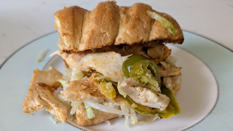 A toasted white sub hoagie roll is topped with cajun-seasoned grilled chicken, jalapenos, cheese, and shredded lettuce on a blue and white plate