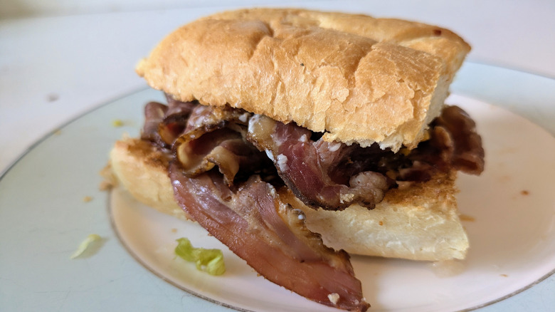 A white hoagie roll is toasted and topped with sliced beef brisket on a blue and white plate with some crumbs and shredded lettuce visible