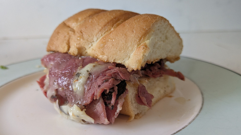Pastrami and corned beef are piled on a toasted white sub hoagie roll and topped with melted cheese on a blue and white plate.