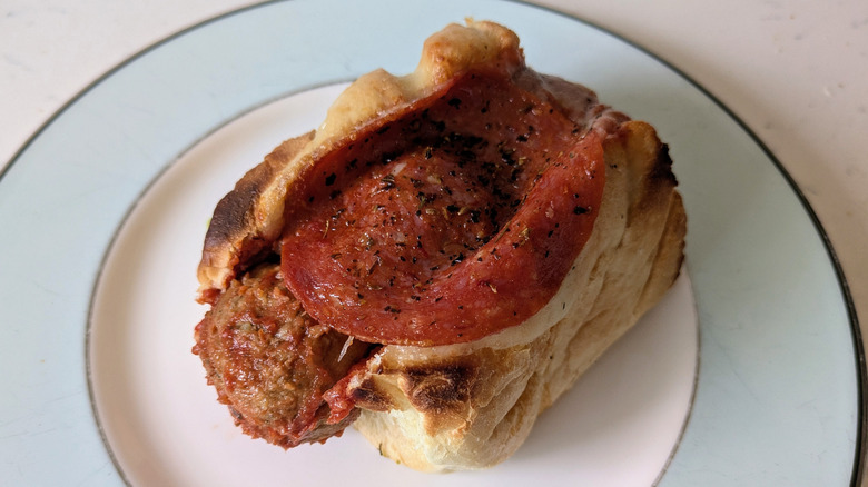 A toasted garlic butter sub hoagie roll is topped with Italian meatballs, red marinara sauce, cheese, and large pepperonis, dusted with Italian seasoning and toasted together