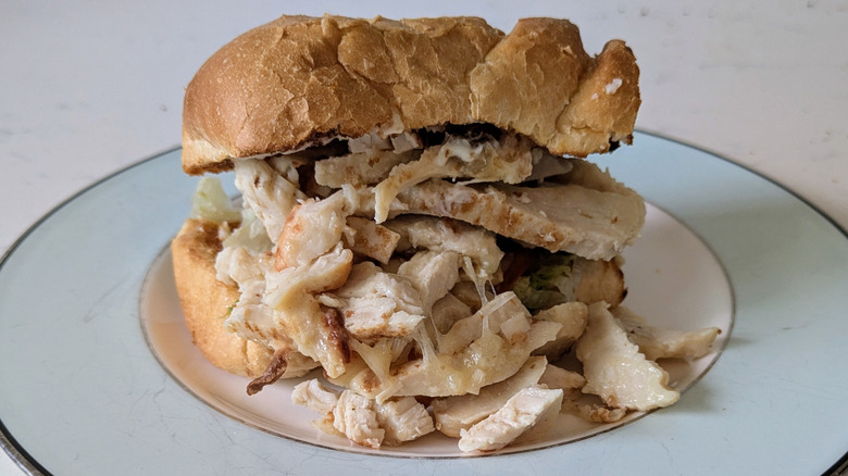 A blue and white plate features a toasted white hoagie roll overflowing with grilled chicken breast and cheese. No other toppings are visible.